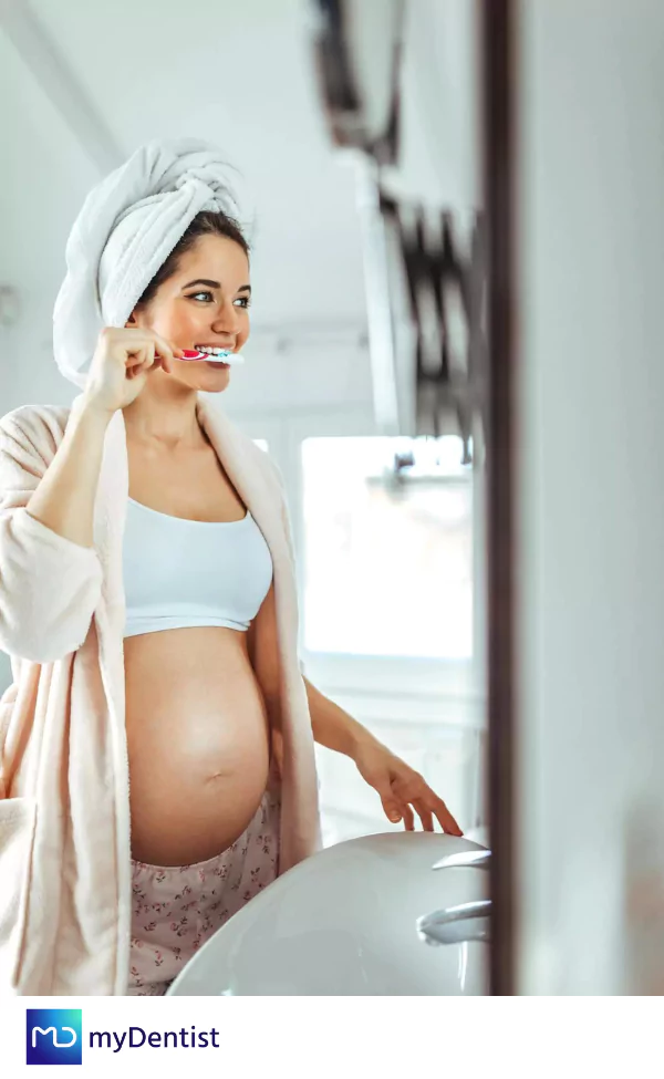 mujer embarazada en el baño frente al espejo con toalla en la cabeza cepillándose los dientes para prevenir la gingivitis en el embarazo